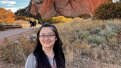 smiling woman, posing with a dog, rocky mountain in the background