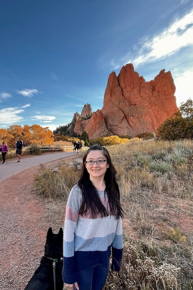 smiling woman, posing with a dog, rocky mountain in the background