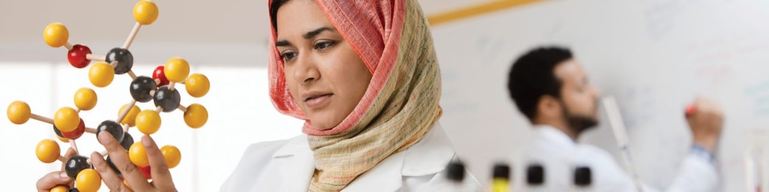 Mixed race scientist in hijab looking at molecule model