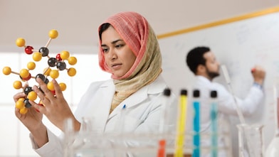 Mixed race scientist in hijab looking at molecule model
