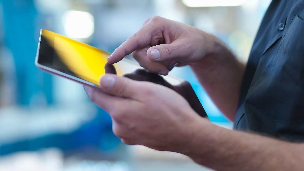 Person operating a touchscreen smartphone in an industrial setting.