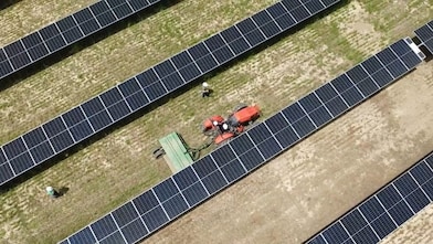 overhead view of farming tractor pulling a combine between rows of solar panels.