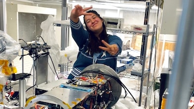 woman in a lab, with her hands in air making a peace sign