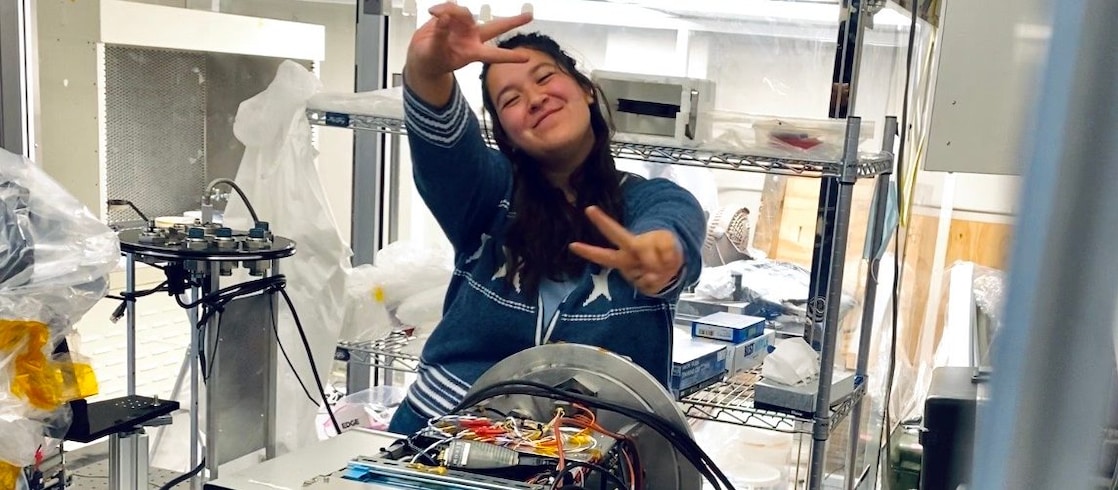 woman in a lab, with her hands in air making a peace sign 