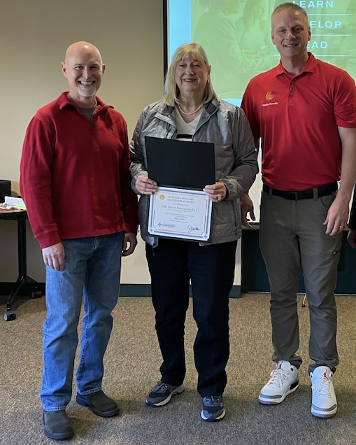 group of people standing in front of screen. Woman is holding a certificate.