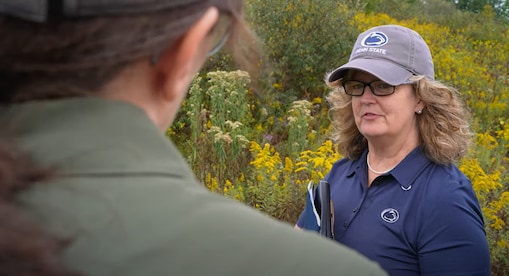 woman in hat and blue shirt speaking to a colleague