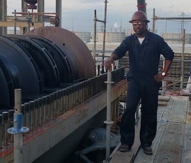 A man stands in protective gear next to a refining unit