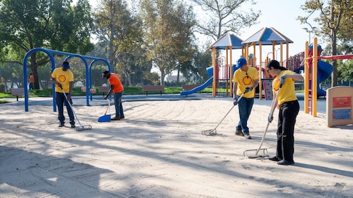 people in yellow shirts raking sand in a playground