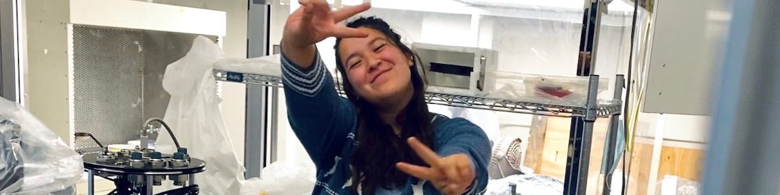 woman in a lab, with her hands in air making a peace sign