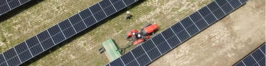 overhead view of farming tractor pulling a combine between rows of solar panels.