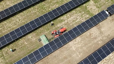 overhead view of farming tractor pulling a combine between rows of solar panels.