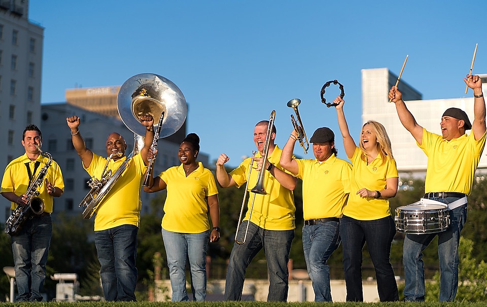 Shell Louisiana musicians in yellow shirts, holding their instruments celebrate making music.