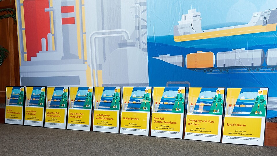 Nine Community Grants award plaques are lined up in front of Shell banner