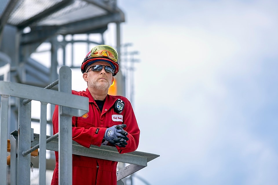 Man in a hardhat and safety glasses leans over an industrial unit.