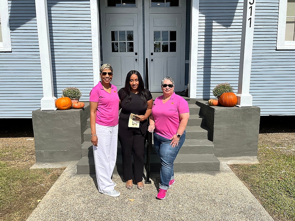 Three women smile in front of a newly opened education and family-history center.