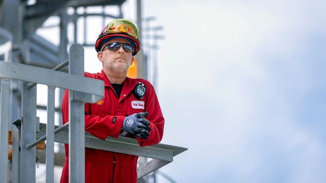 Man in a hardhat and safety glasses leans over an industrial unit.