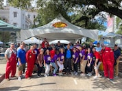 A large group of people pose in front of their company tent for a jambalaya cook-off, a non-profit event.