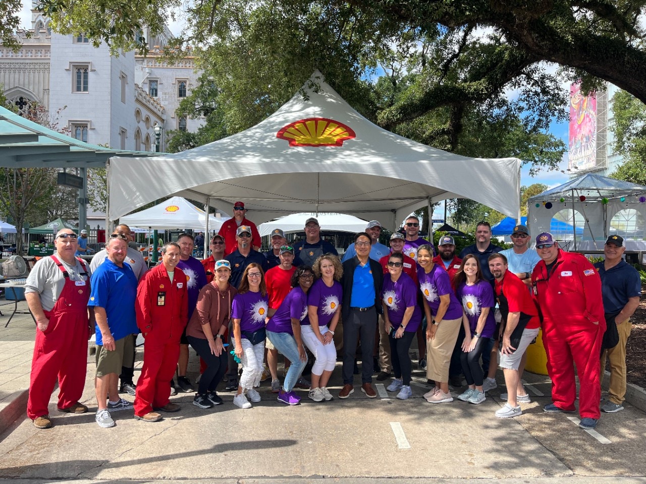 A large group of people pose in front of their company tent for a jambalaya cook-off, a non-profit event.