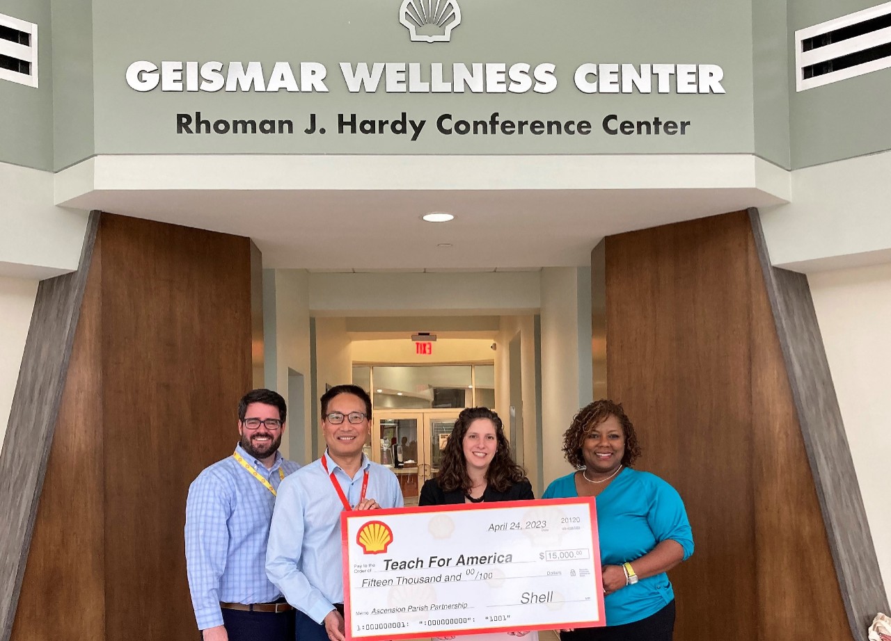 Four people smile while presenting a check of $15,000 to Teach for America.