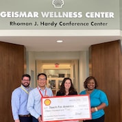 Four people smile while presenting a check of $15,000 to Teach for America.