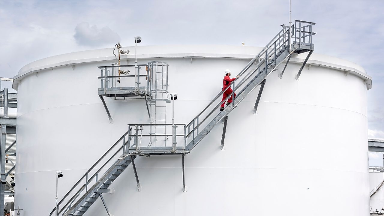 An employee in a red jumpsuit climbs the stairs of a unit tank.