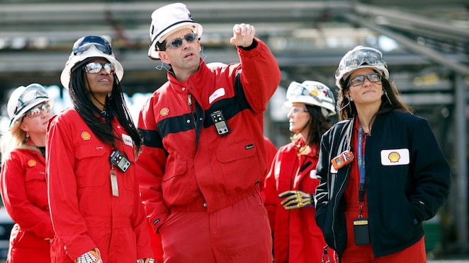 Shell team members in red coveralls and helmets, along with Secretary Giacometto, stand together at the Norco site, with one person pointing off-camera during a discussion or inspection.