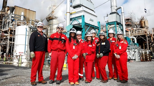 Eight Shell Norco employees, joined by Secretary Giacometto, in red protective gear stand in the facility in front of a large industrial structures and equipment.