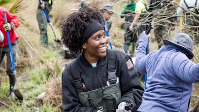 Volunteers in waders and gloves work in a marshy area, using tools to plant trees at Wetland Watchers Park in St. Charles Parish, Louisiana.