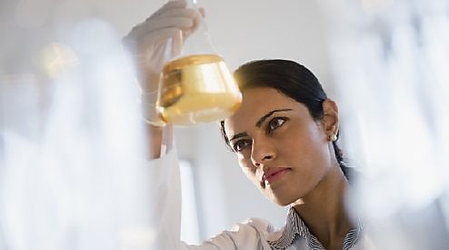 Lab technician looking at a glass vial that holds lubricant