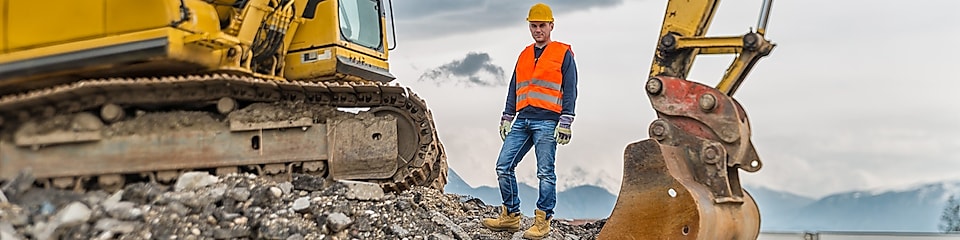 Man wearing a safety suit close to an excavator