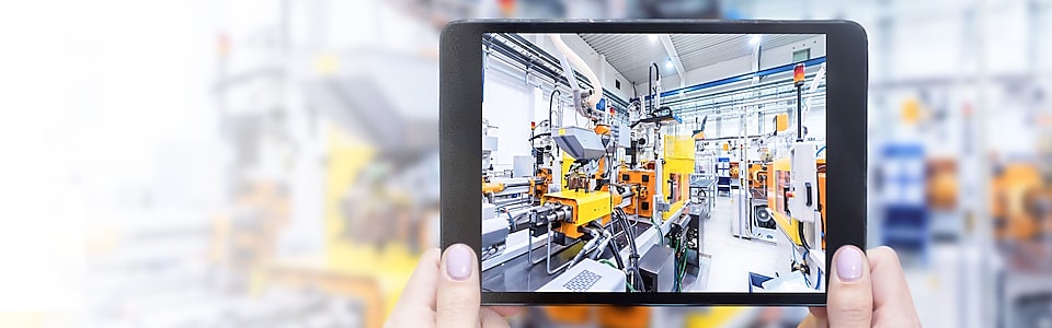 Close-up of hands holding a tablet and a view of machinery in the tablet screen
