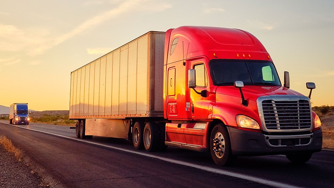 Two commercial transport semi-trucks driving on a remote highway.