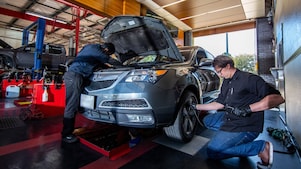 Two technicians at a service & tire shop working on a mid-size SUV to perform an oil change and check the tire pressure.