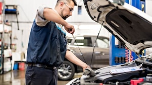 A technician at a dealership shop working in the hood of a car.
