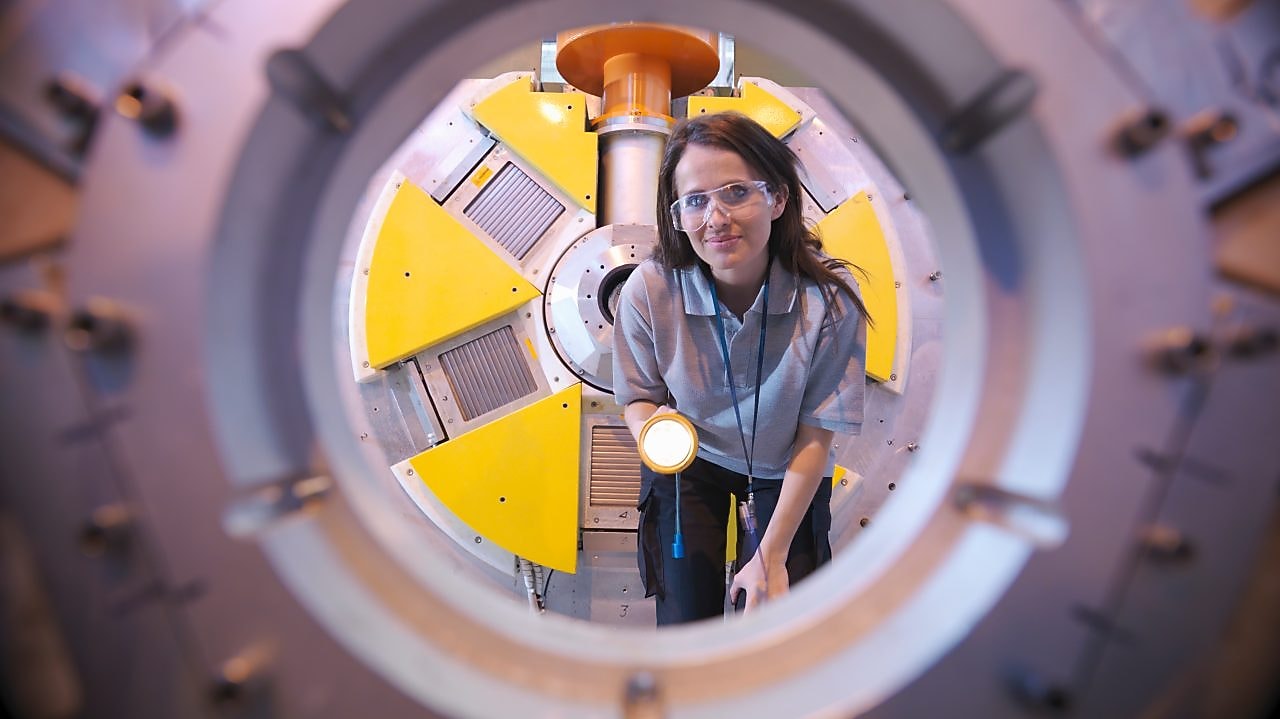 A woman inspects the inside of machinery equipment with a torch