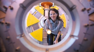 A woman inspects the inside of machinery equipment with a torch