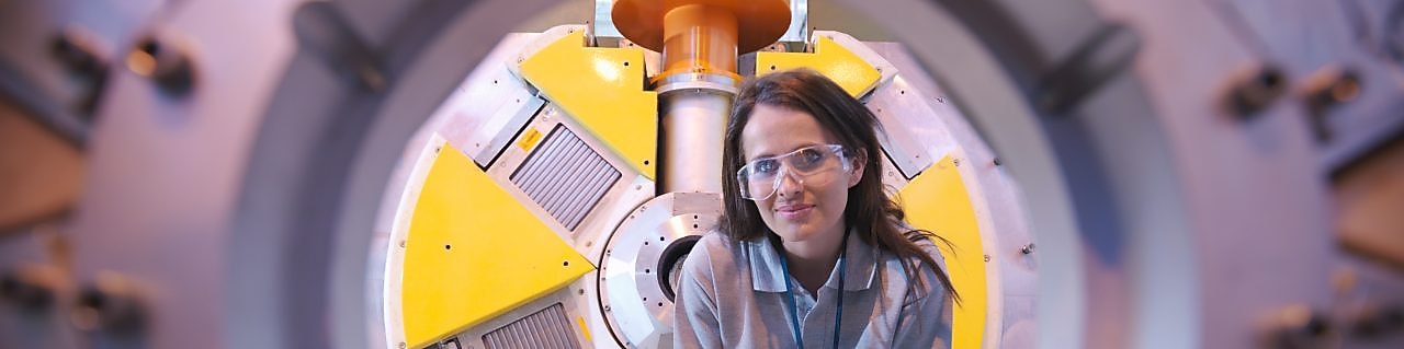 A woman inspects the inside of machinery equipment with a torch