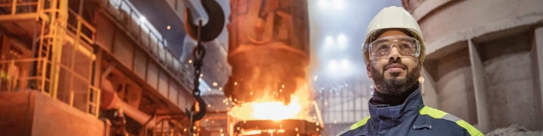 Worker in full PPE facing forward with furnace in the background