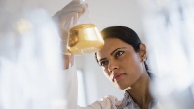 Lab technician looking at a glass vial that holds lubricant