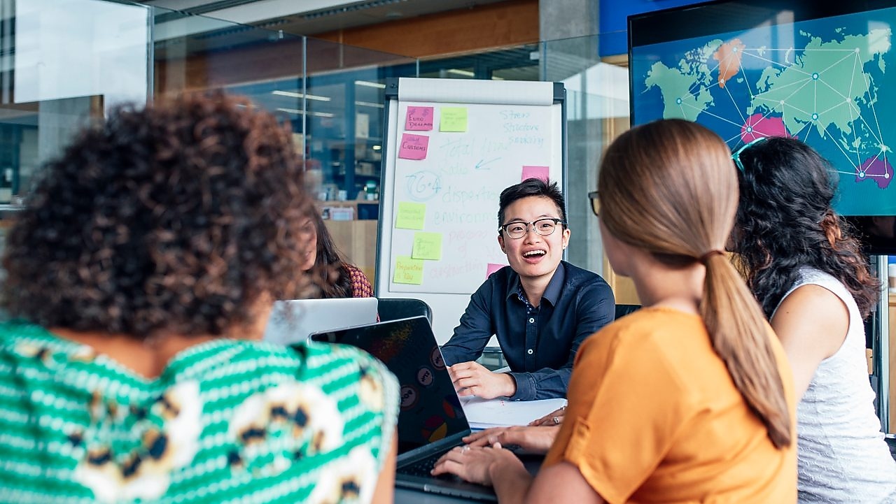 Four business people sitting around a round table reading documents, grey and yellow carpet