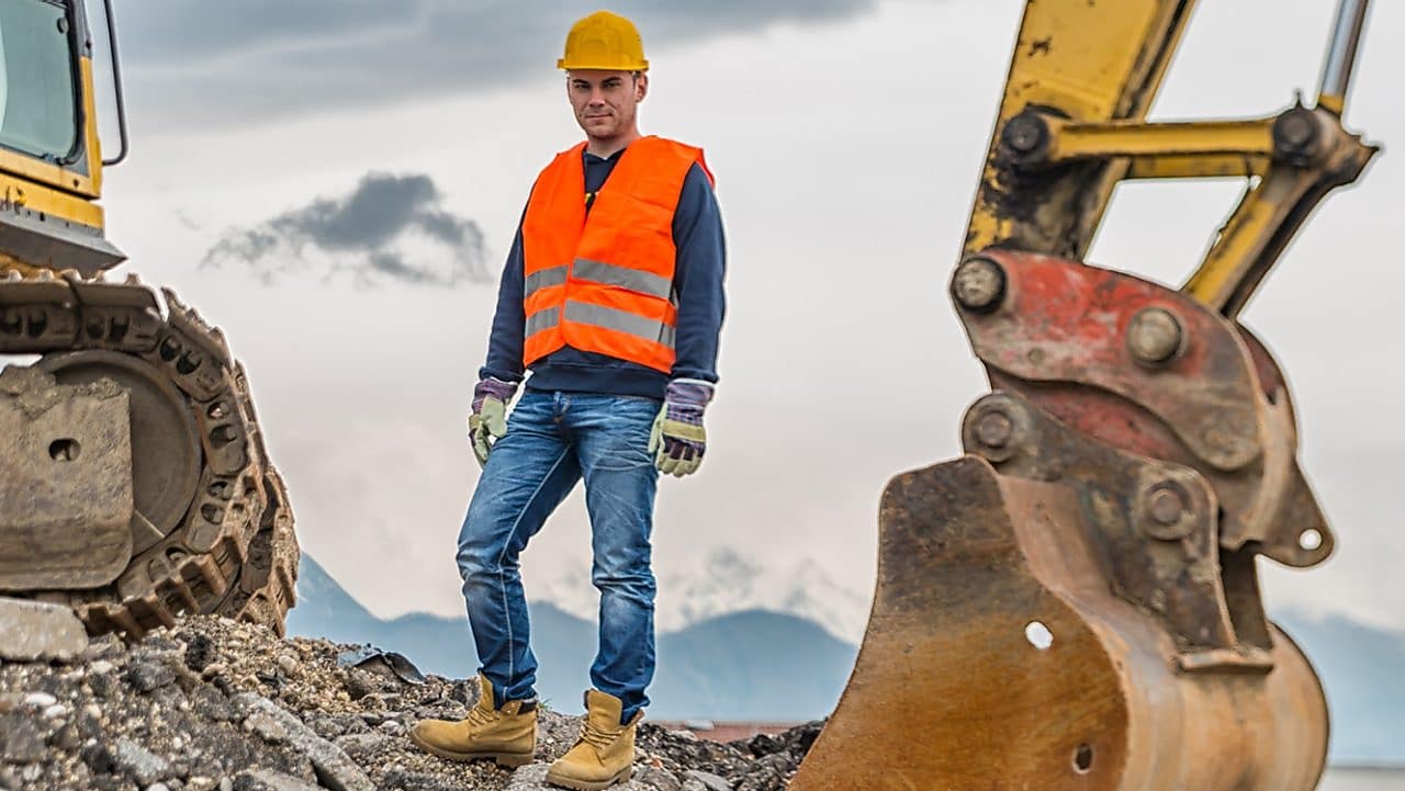 Man wearing a safety suit close to an excavator