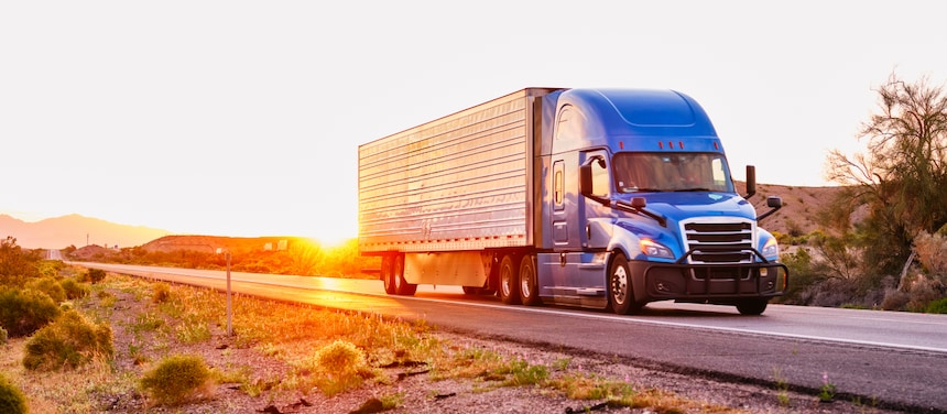Blue semi-truck traveling on a highway at sunset