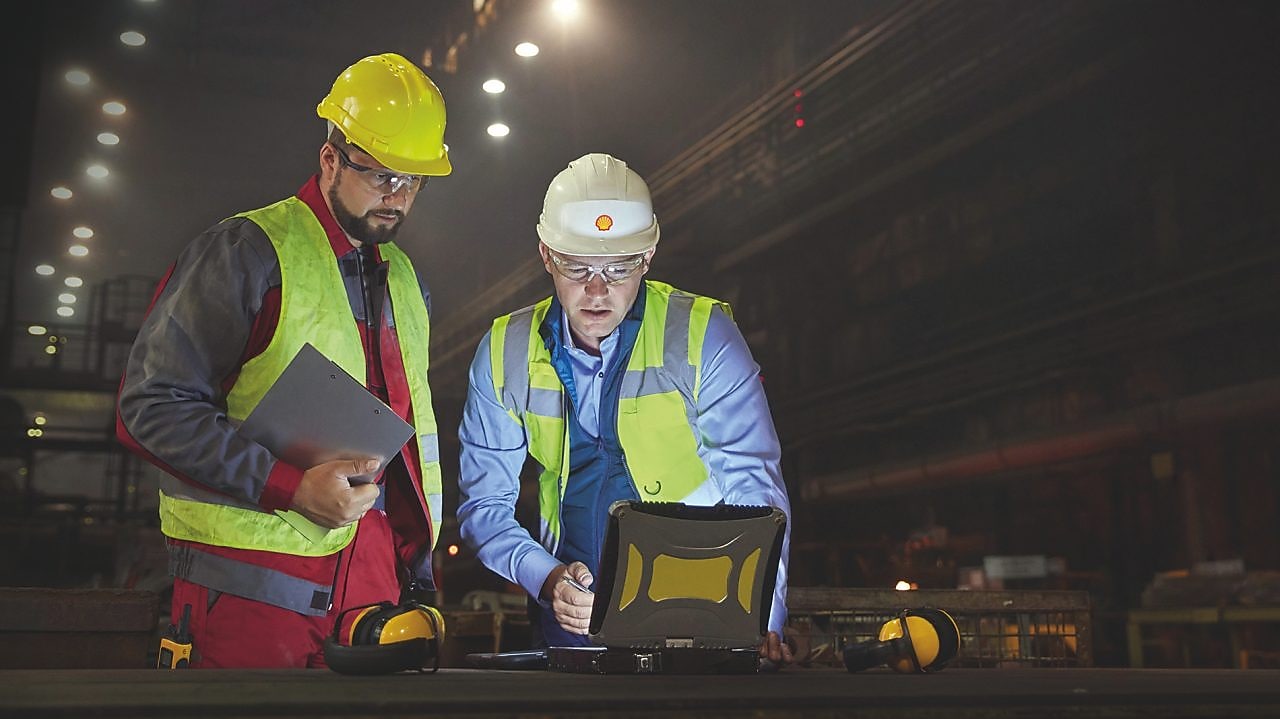 Steelworkers using laptop in dark steel mill
