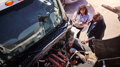 Two people inspecting truck engine