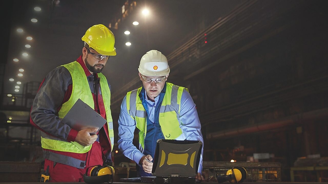 Steelworkers using laptop in dark steel mill