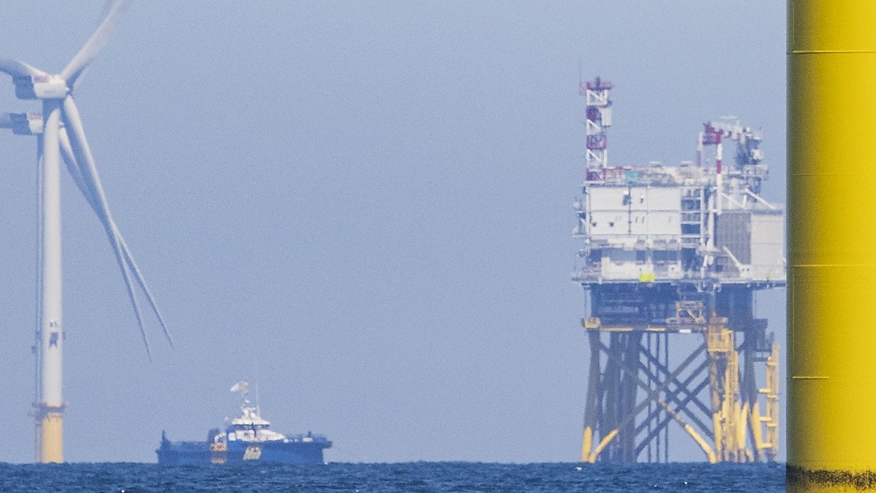 An offshore substation next to a wind farm and service vessel.