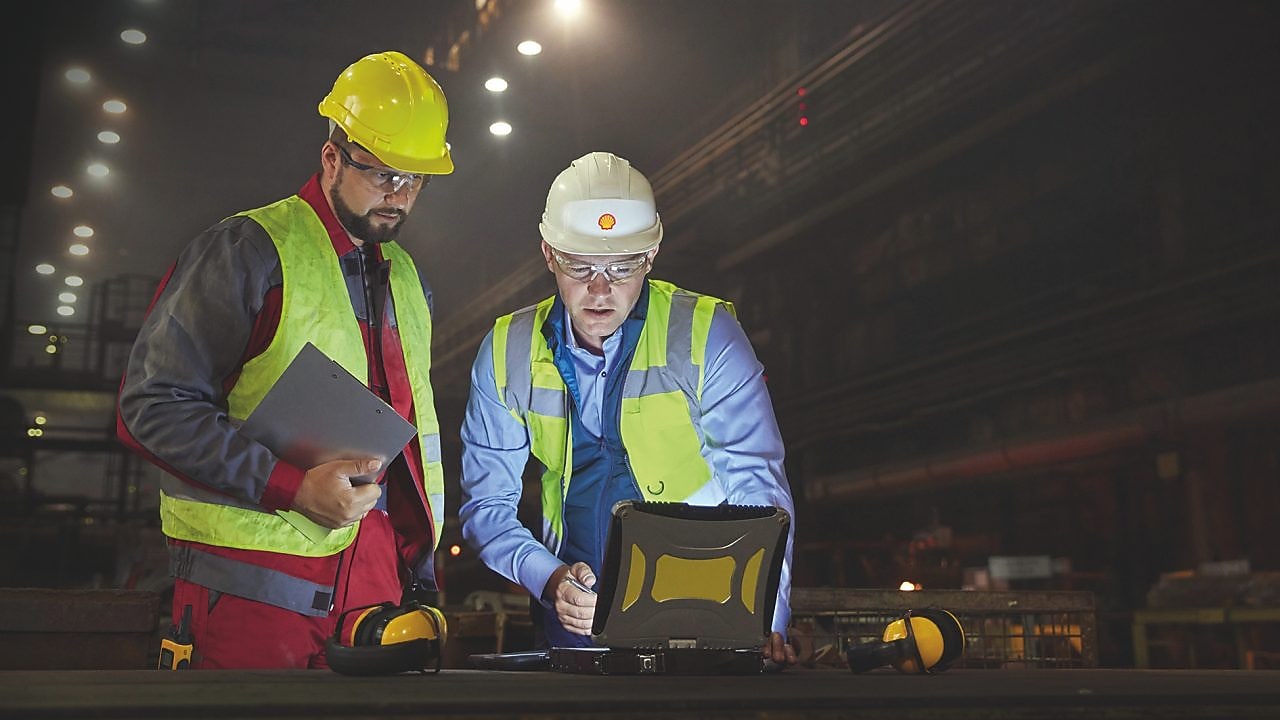 Steelworkers using laptop in dark steel mill