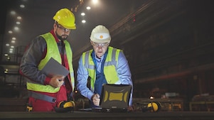 Steelworkers using laptop in dark steel mill