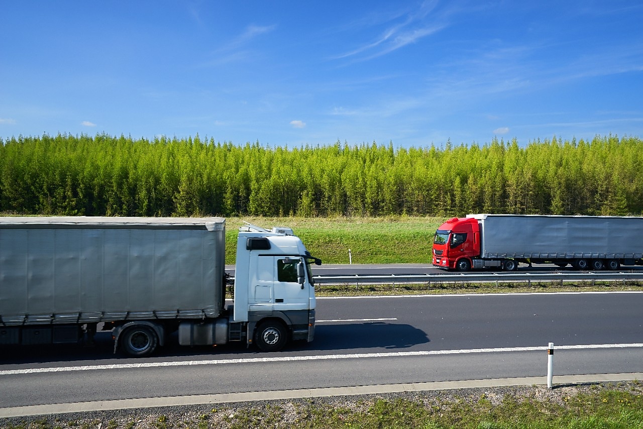 two trucks on a road with a forest on the background