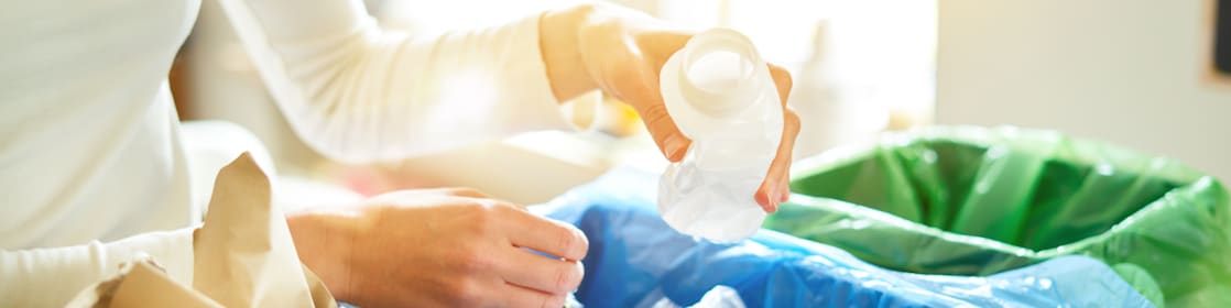 Individual recycling plastic bottle into blue-labeled recycling bin at home
